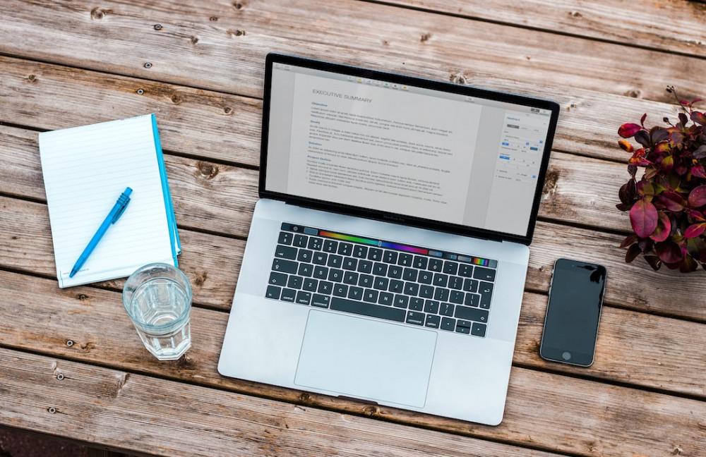You website is a business treat as such Laptop on wodden table with mobile, glass of water, pen and paper and plant