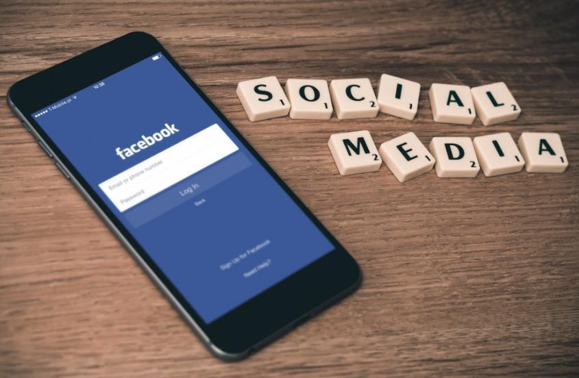 Phone with words words of FaceBook in blue screen plus words of social media on brown desk Phone with words words of FaceBook in blue screen plus words of social media on brown desk