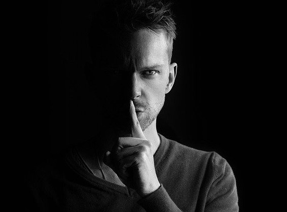 Man with finger to mouth on black Background. Whispering what goes on in the Office stays in the Office What is said in the Office stays within the Office